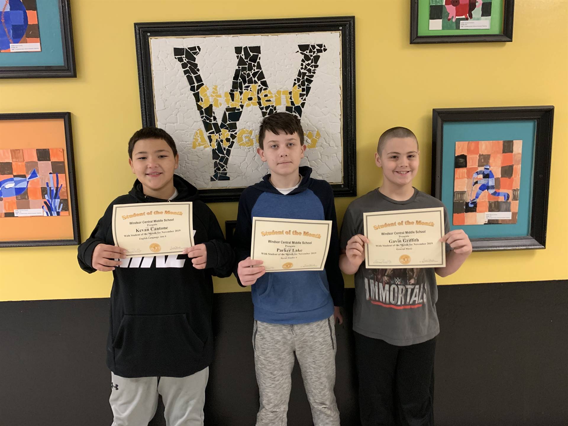 Three students holding certificates in front of a wall