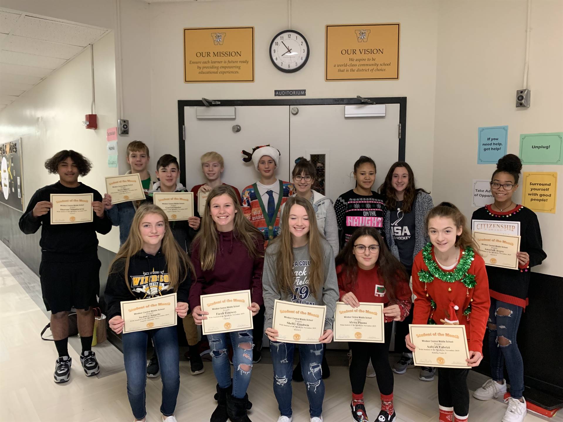 Two rows of 8th grade students holding certificates in a hallway
