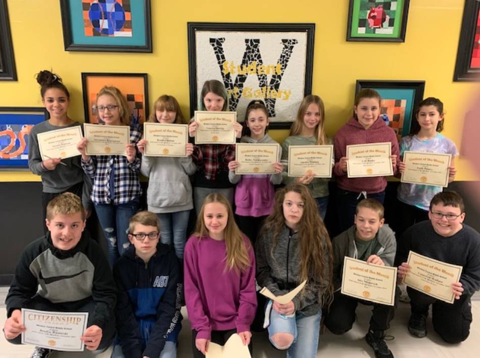 Two rows of 7th grade students holding certificates in front of a wall