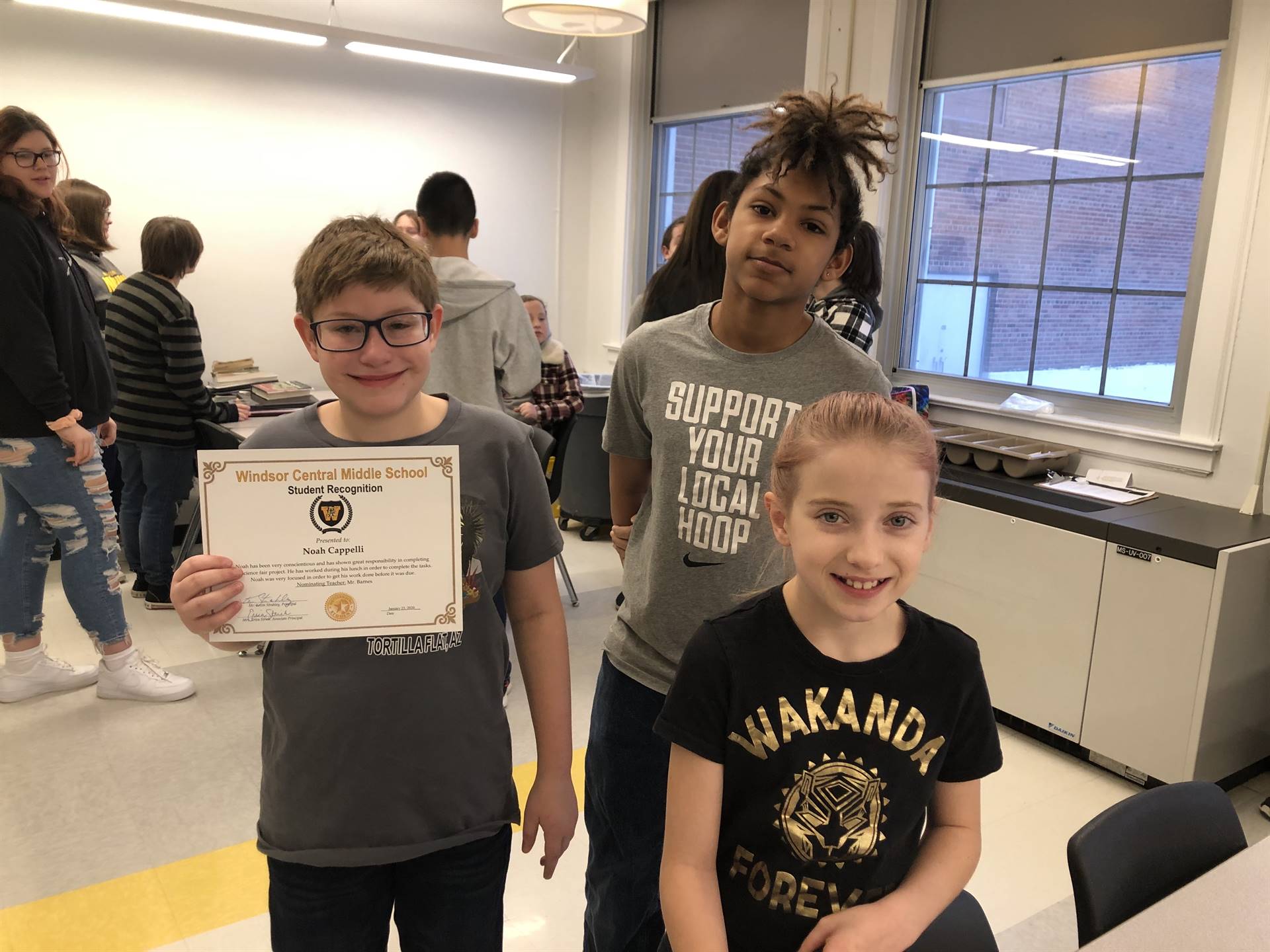 Two boys, one holding a certificate, and a girl standing