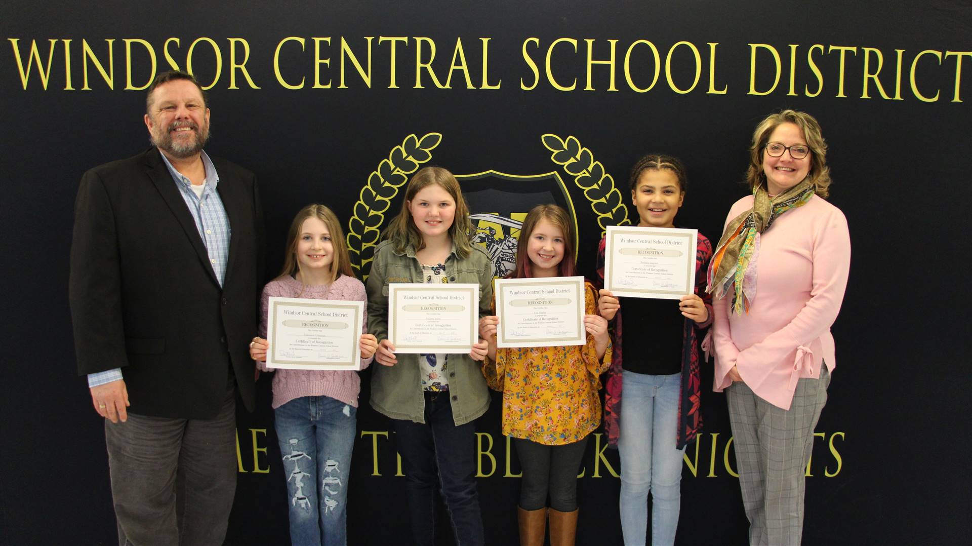 four children holding certificates flanked by an adult on each side. 