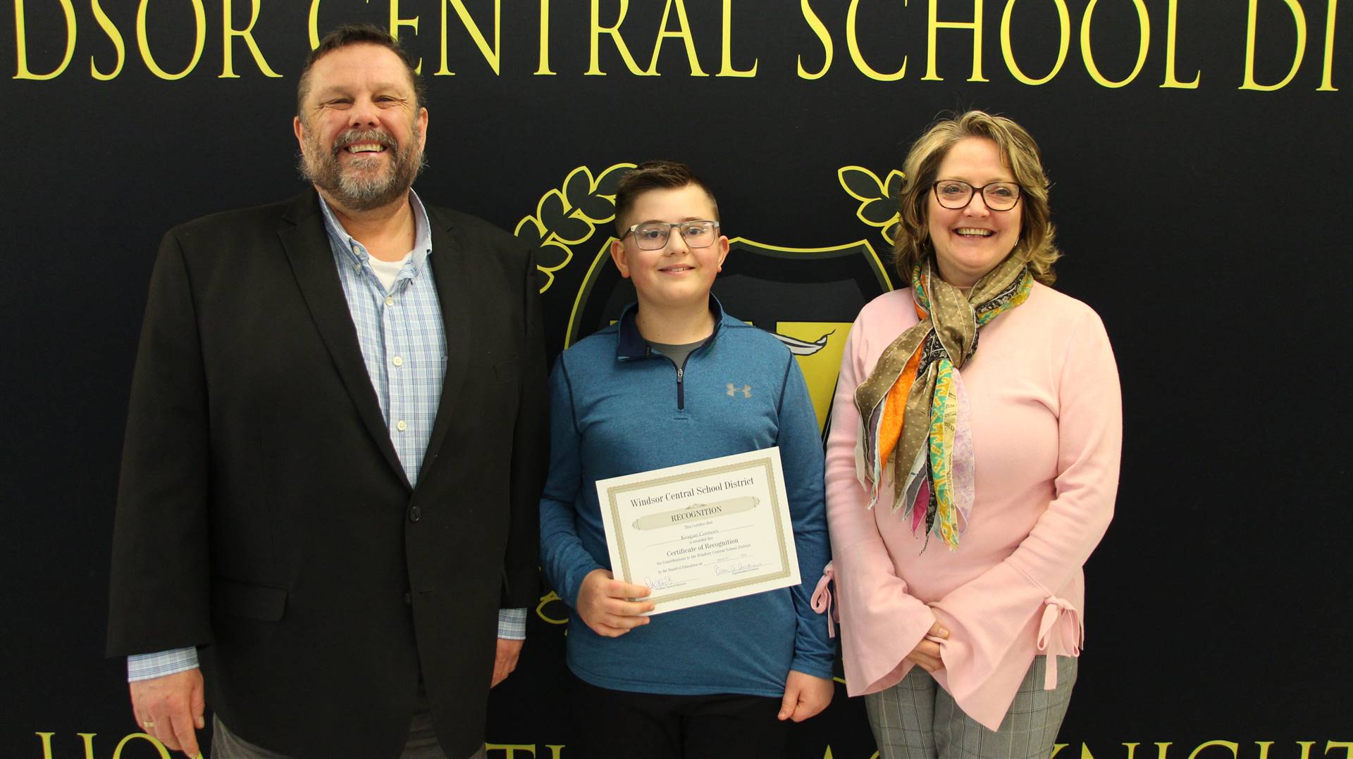 Boy holding a certificate with an adult on each side