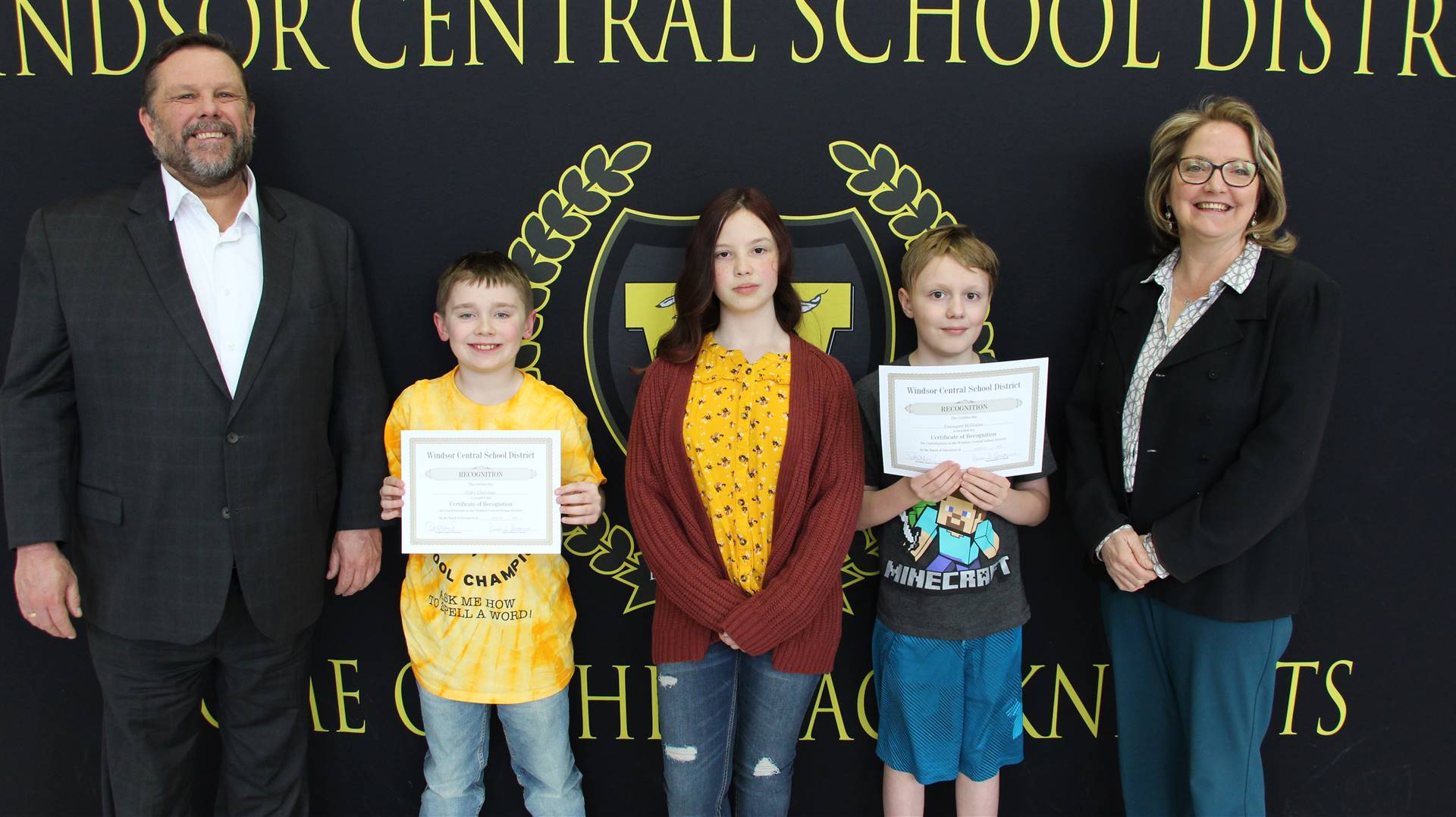 Three children and two adults standing in front of a banner