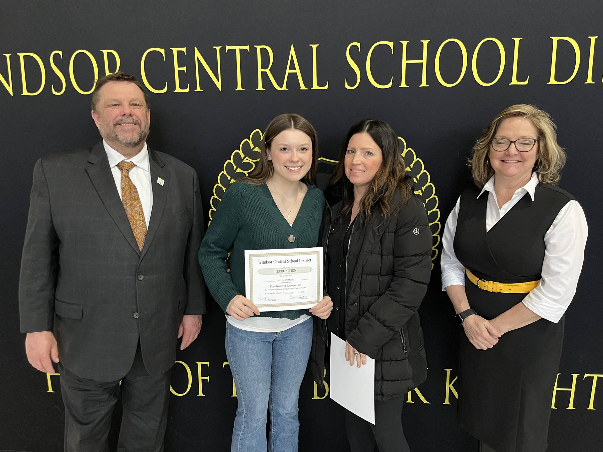 Pete Nowacki, Erin Thomas-Allen, Isabella De Wolfe, and Margo Kibbler standing in front of a banner 